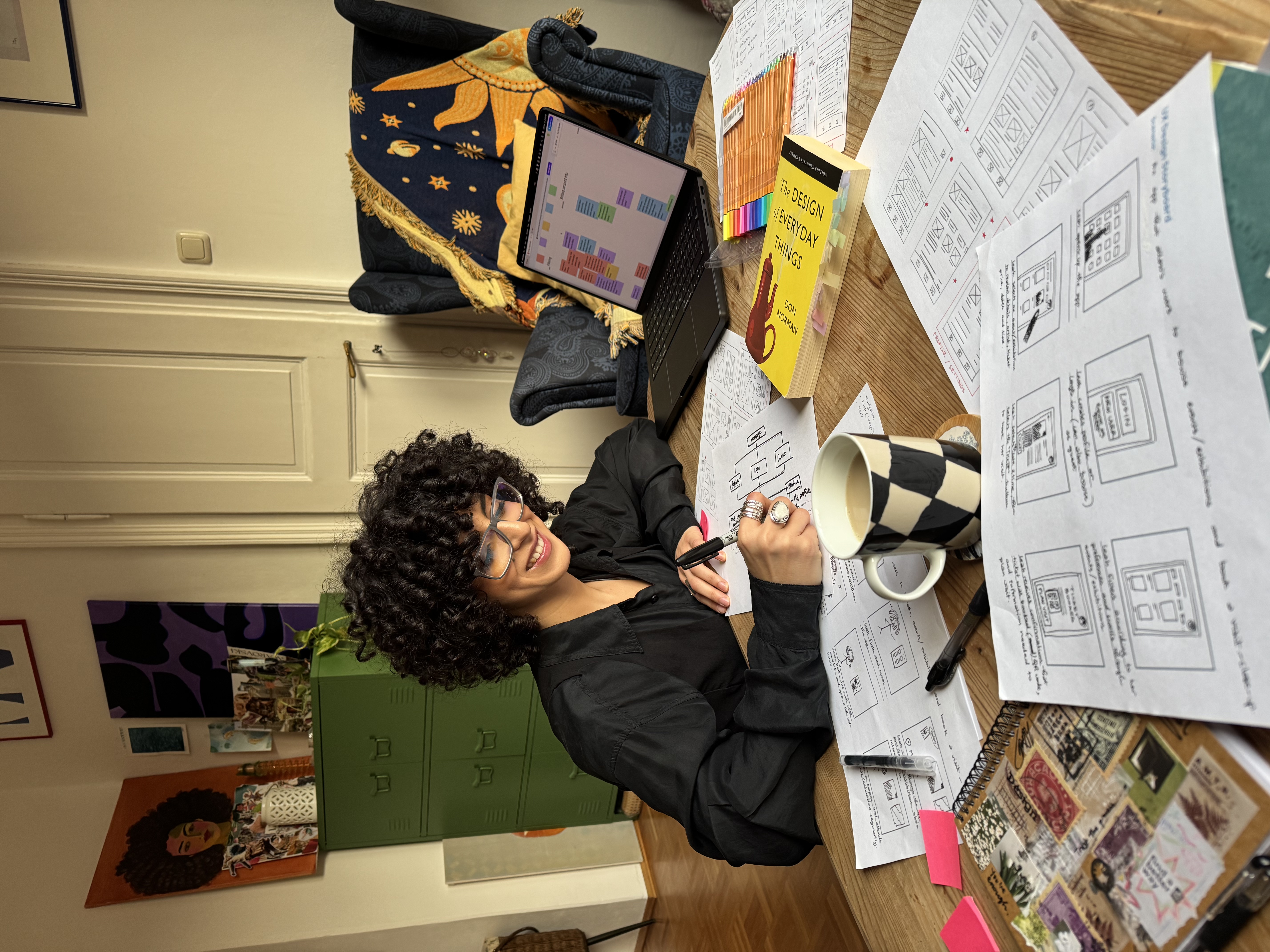 Ichrak working on information architecture, surrounded by storyboards and wireframes, smiling.